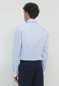 Helles blaues Hemd mit langen Ärmeln, Knopfmanschetten und klassischem Kragen. Glattes Material, taillierte Passform und Rückenpasse.