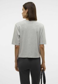 Grijze cropped t-shirt met korte mouwen, gemaakt van zachte stof. Heeft een ronde halslijn en een rechte zoom. Gecombineerd met zwarte broek.