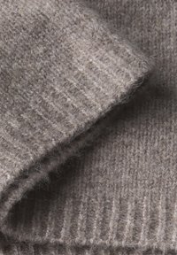 Tissu en laine tricoté de couleur beige doux avec une texture côtelée, présentant une surface épaisse et douillette avec des éclats légers pour un détail supplémentaire.