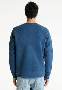 Sweatshirt albastru dintr-un material elastic, cu guler rotund și manșete ribbate. Fără logo-uri sau modele vizibile, cu o textură netedă.