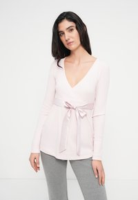 Μακρυμάνικη γαλάζια μπλούζα με βαθύ ντεκολτέ σε σχήμα V και σατέν κορδόνι στη μέση. Συνδυασμένο με γκρι παντελόνι, με λεία υφή.