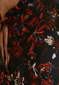 Svart tyg med ett blommönster i rött, orange, blått och vitt. Har en knytning vid halsringningen och en mjuk textur.