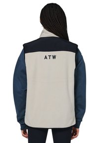 Fleece ærmeløs jakke i creme med marineblå skuldersektion, prydet med "ATW" broderi. Struktureret stof, løs pasform og farveblok design.