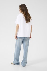 T-shirt blanc oversize en coton, avec des manches courtes et un ourlet droit, associé à un jean bleu clair ample et des chaussures décontractées.