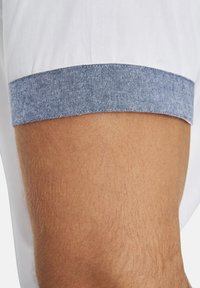 Kurzarmhemd mit weißem Körper und blauen denimmustern Ärmeln. Die Manschette hat eine strukturierte Oberfläche, die im Kontrast zu dem glatten Stoff des Hemdes steht.