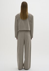 Graues Zweiteiler-Outfit bestehend aus einer verkürzten, boxy Jacke und weit geschnittenen Hosen, gefertigt aus strukturiertem Stoff mit einem neutralen, minimalistischen Design.