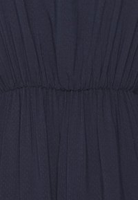 Vestido azul-marinho com tecido texturizado e com bolinhas. Apresenta uma faixa elástica na cintura e um design de saia fluida e pregueada.