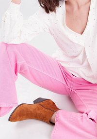 Weiße Bluse mit goldenen Sprenkeln, kombiniert mit knallpinken, weit geschnittenen Jeans. Braune Wildleder-Stiefeletten mit Blockabsatz und seitlichem Reißverschluss.