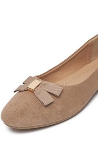 Zapatilla bailarina de ante beige con puntera redonda, detalle de lazo texturizado y adorno de metal dorado en el centro del lazo.