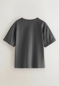 Tamsiai pilkas trumpomis rankovėmis medvilninis marškinėlis, matomas iš nugaros, prieš vientisą šviesią fono.