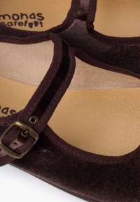 Brązowy welurowy but z paskiem i metalową klamrą. Gładka, miękka tekstura, zaokrąglony nosek i wyściełana wkładka.