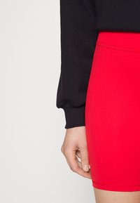 Pantalones cortos rojos de tejido elástico con una textura suave y una cinturilla elástica, combinados con una camiseta negra de manga larga con puños acanalados.