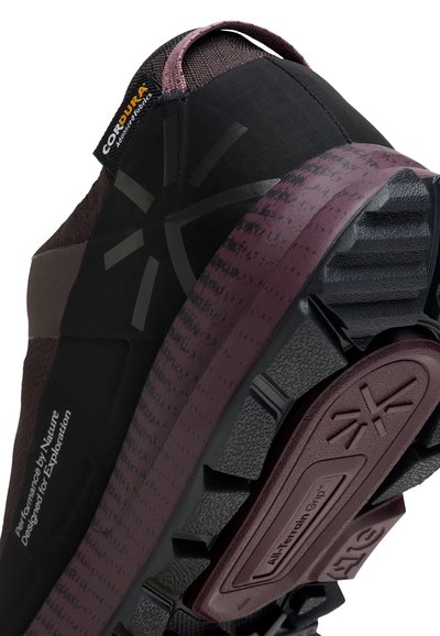 Chaussure de trail noire et marron foncé avec une semelle en caoutchouc texturé, des accents en tissu Cordura et des détails de marque en relief.