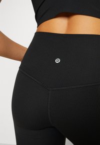 Musta ribbed korkeavyötäröinen legginsit, joissa on pieni logo, valmistettu joustavasta materiaalista, esittelee saumatonta muotoilua ja tekstuuripintaa.
