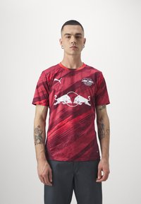 Maglia sportiva rossa realizzata in materiale sintetico con una finitura testurizzata, caratterizzata da un design a gradiente, logo bianco e accenti corallo.