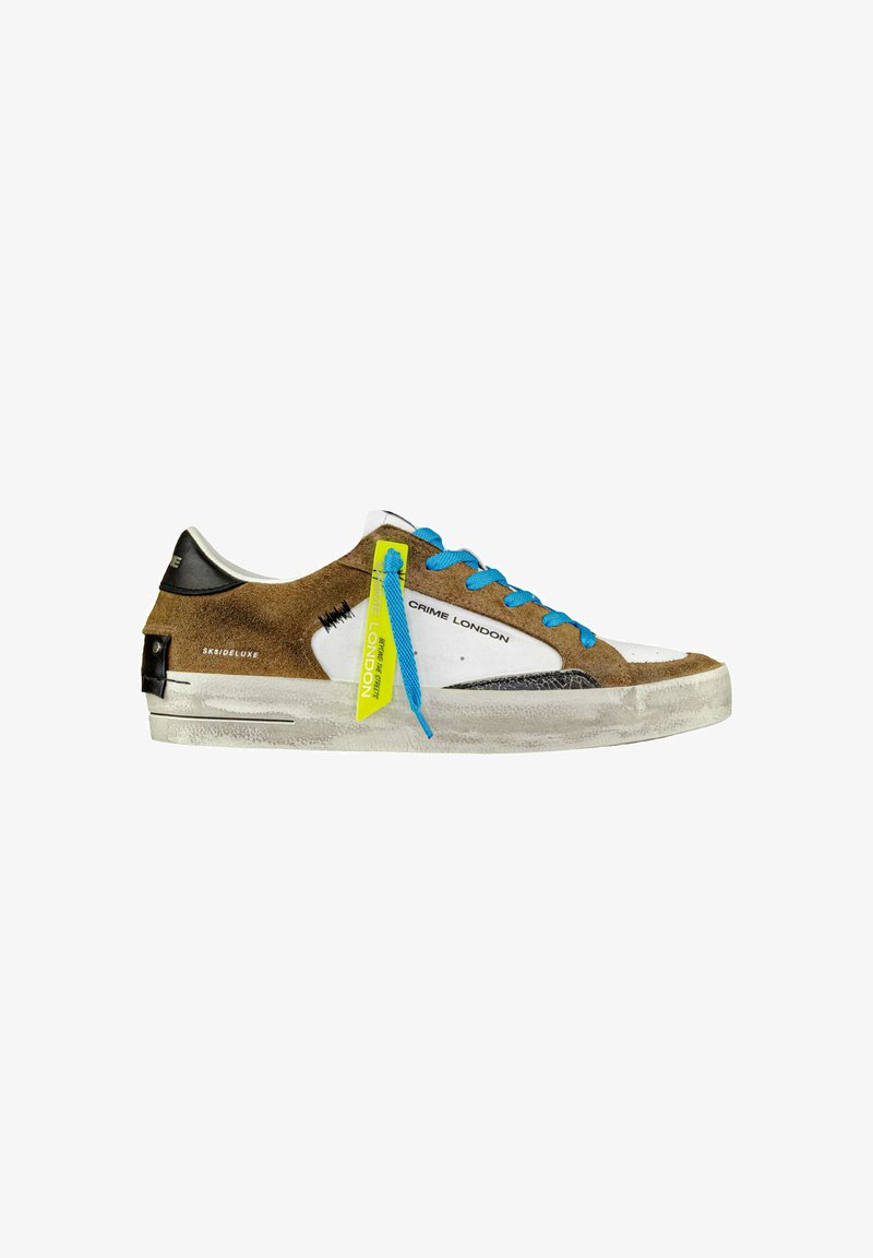 Sneaker in suede marrone con lacci blu e dettagli bianchi. Presenta un parafango nero, suola in gomma bianca e un'etichetta gialla neon.