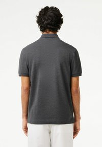 Mörkgrå polo skjorta med korta ärmar, en plan krage och en texturerad tygfinish. Bakifrån syns minimala sömnadsdetaljer.