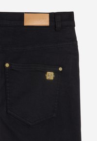 Mustat farkut, joissa on takatasku, jossa on kultaiset niitit ja pieni kultainen embleemi, sekä vyötäröllä vaaleanruskea nahkainen merkintä, jossa lukee "FREDDY".