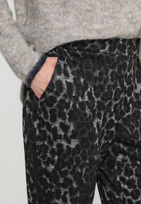 Zwarte broek met een luipaardprintdesign in grijs en donkerbruin, gemaakt van zachte, gestructureerde stof, met zijzakken.