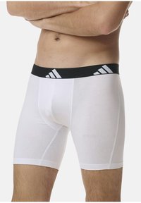 Weiße Boxer-Briefs mit einem schwarzen elastischen Bund, der drei weiße Streifen aufweist. Glatte Textur, moderat taillierter Schnitt.