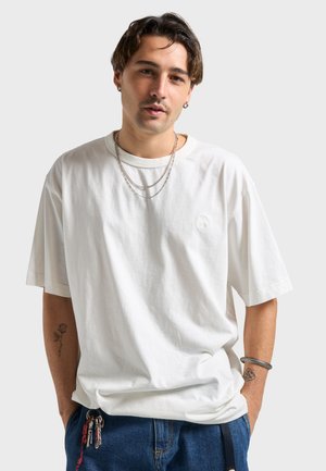 Hvid bomuld t-shirt med korte ærmer, løs pasform og et lille logo på brystet. Bruges med lagdelte sølvkæder og denimjeans.