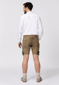 Brown leather shorts with decorative blue buttons on the sides, paired with a white long-sleeve shirt. Wooden shoes and knitted socks.