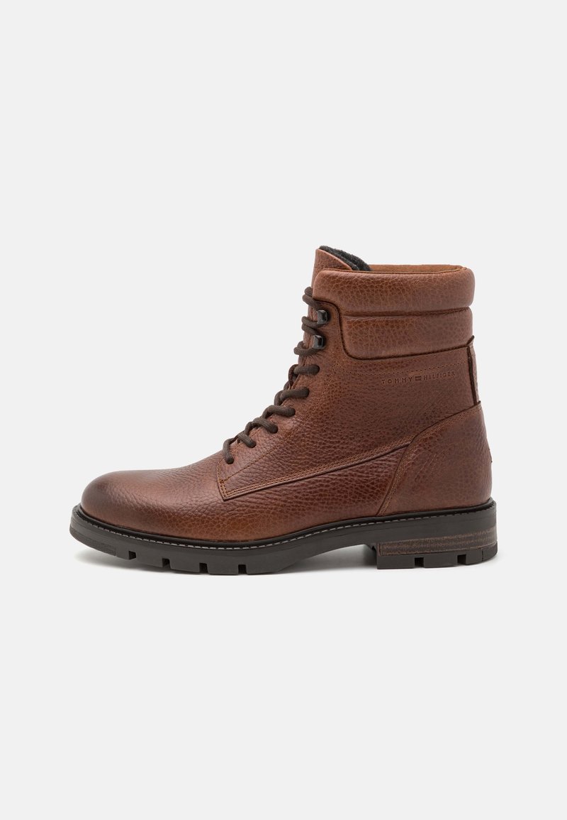 Bottine montante en cuir marron à lacets, col rembourré et semelle gomme noire à crampons, côté embossé du nom de la marque.