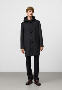 Kolenwollen jas met een capuchon, togglesluitingen, opgestikte zakken en een rechte snit, gecombineerd met donkere broeken en bruine instappers.