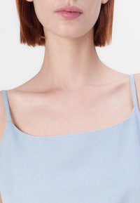 Jasnoniebieski top na ramiączkach z cienkimi paskami, wykonany z gładkiego, miękkiego materiału, z prostym dekoltem, zaprojektowany w minimalistycznym stylu.