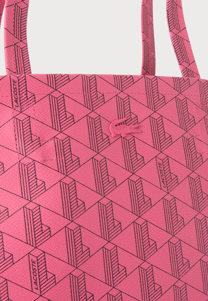 Pink textured tote bag with geometric black line patterns, Lacoste brand name, and a small crocodile logo in matching pink.