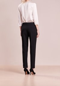 Pantalons ajustés noirs avec une coupe slim, fabriqués à partir d'un tissu lisse, dotés d'une taille basse et de poches arrière, associés à des chaussures à talons hauts.