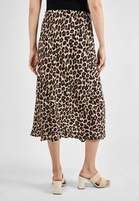 Midi sukňa s leopardím vzorom v béžovej a čiernej farbe, vyrobená z ľahkého materiálu. Má voľný strih a rozšírený lem. Skombinovaná s béžovými sandálmi na blokovom podpätku.