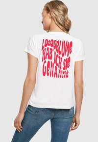 Hvid bomuld t-shirt med fed rød tekst på ryggen, der står "Lotosblume hab' ich sie genannt." Korte ærmer og afslappet pasform.