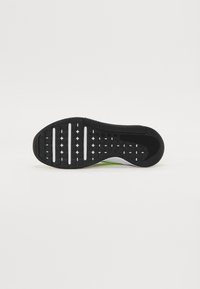 Zwarte sportieve schoenzool met een tactiele rubberen oppervlak, noppen voor grip, en een witte tussenzoolaccent met groene details.
