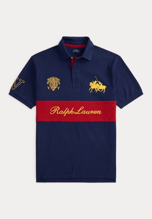 Sötétkék galléros póló piros vízszintes csíkkal, sárga Ralph Lauren felirattal, hímzett pólójátékos logóval és címerrel a mellrészen és az ujjon.