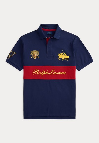 Μπλε ναυτικό πόλο πουκάμισο με κόκκινη οριζόντια ρίγα, κίτρινη επιγραφή Ralph Lauren, κεντημένο λογότυπο παίκτη πόλο και έμβλημα με ασπίδα στο στήθος και το μανίκι.