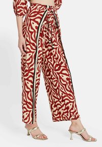Pantalones de pierna ancha en una base crema con un patrón abstracto rojo, que cuentan con una franja lateral negra y una cinta de tela en la cintura.