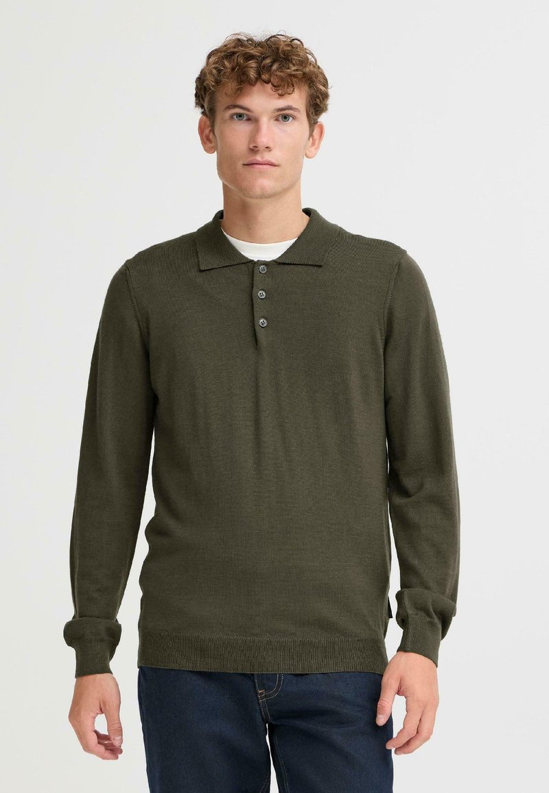 Polo a maniche lunghe di colore verde oliva con colletto a coste, tre bottoni e polsini aderenti, realizzato in un tessuto a maglia texturizzata.