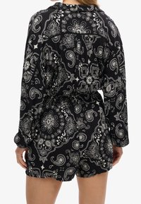 Monos de color negro con estampado de paisley blanco, mangas largas, cintura con cordón y dobladillo con forma de concha. Tejido texturizado con un corte relajado.