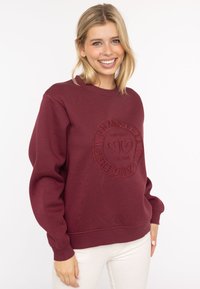 Burgundowa bluza z okrągłym dekoltem z wytłaczanym wzorem z napisem "POZOSTAŃ DZIKI I WOLNY, ZAŁOŻONA W 2014 R." Miękka tekstura z prążkowanymi mankietami i dołem.