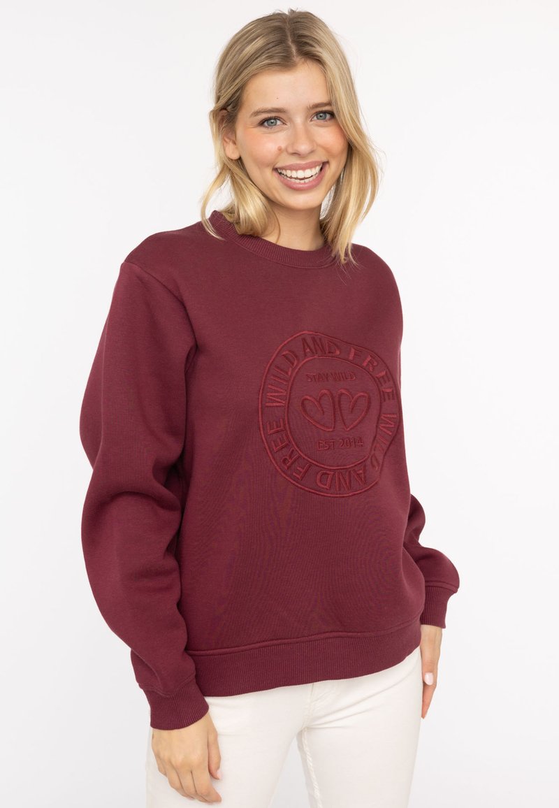 Burgundowa bluza z okrągłym dekoltem z wytłaczanym wzorem z napisem "POZOSTAŃ DZIKI I WOLNY, ZAŁOŻONA W 2014 R." Miękka tekstura z prążkowanymi mankietami i dołem.