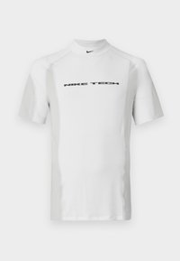White short-sleeve sports shirt with a high collar, featuring a black "NIKE TECH" logo across the chest and contrasting textured panels.