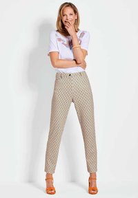 Camicia bianca a maniche corte con ricami colorati, abbinata a pantaloni beige a fantasia con forme a goccia in blu e arancione. Sandali arancioni.