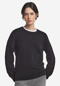 Czarny sweter z dzianiny z okrągłym dekoltem w biały ściągacz, długimi rękawami oraz ściągaczami na mankietach i u dołu. Widoczna miękka struktura.