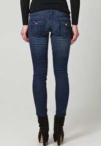 Smala mörkblå denimjeans med hög midja, två bakfickor med metalliska detaljer och en subtil blekningseffekt på benen.