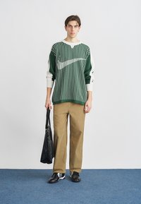 Žalios ir baltos dryžuotos megztos megztinis su ilgomis rankovėmis, smėlio spalvos kelnės, juodi batai ir juoda rankinė. Paprastas dizainas; tekstūra atrodo minkšta.