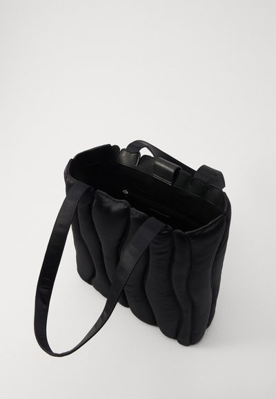 Sac fourre-tout noir matelassé avec deux poignées plates, en matériau satin doux, texture ondulée et ouvert en haut ; l'intérieur comprend une poche zippée.