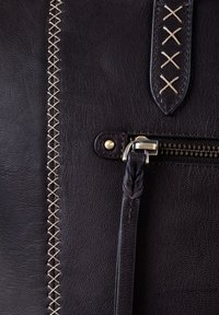 Dark leather bag featuring a textured surface, contrasting beige stitching, a zippered pocket, and a braided leather pull tab.