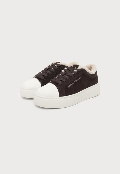 Paire de baskets en daim noir avec semelles en caoutchouc blanc, bouts blancs, lacets noirs et doublure peluche beige clair à l'intérieur.