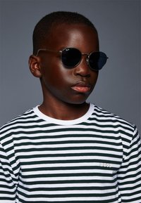 Occhiali da sole rotondi con lenti scure e montatura metallica sottile, abbinati a una maglietta a righe verdi e bianche con un piccolo logo "BOSS".